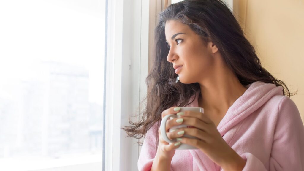 Woman looking at the window with a cup of coffee in hand.